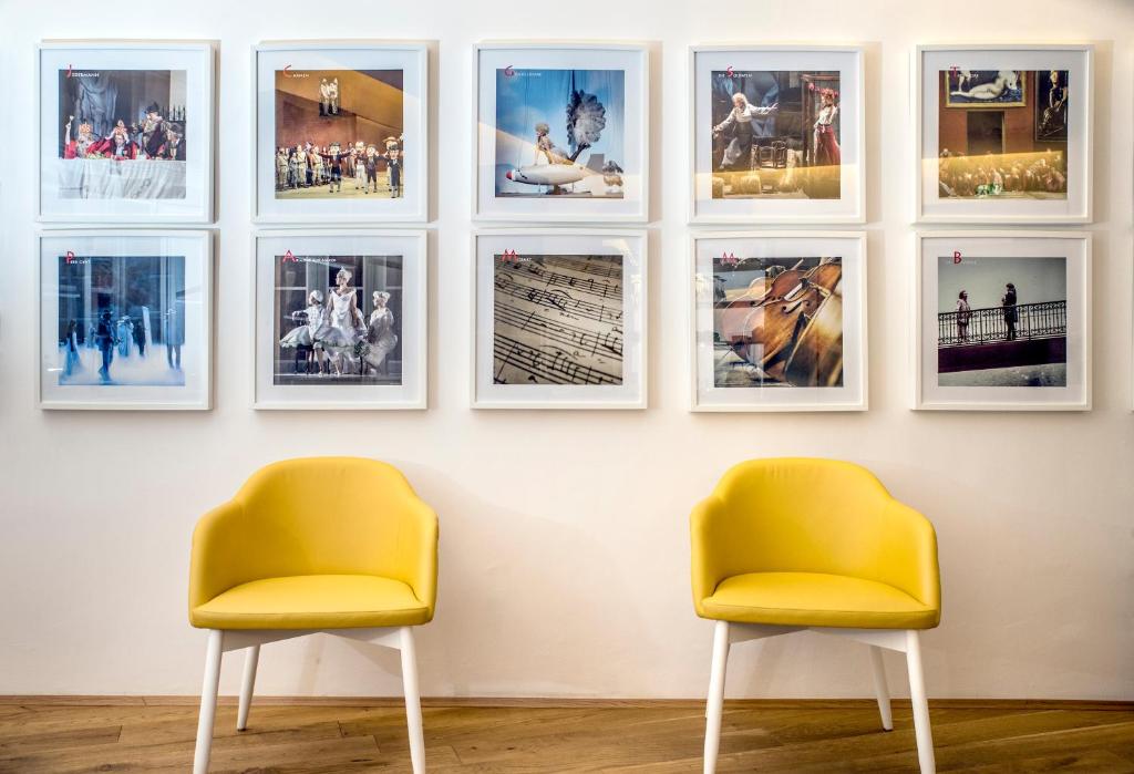 Unique Boutique Hotels in Salzburg 34 Two yellow chairs sit against a white wall, above which are nine framed photos. Reminiscent of Boutique Hotels in Salzburg, the images of performers and musical instruments create an artistic and inviting atmosphere.