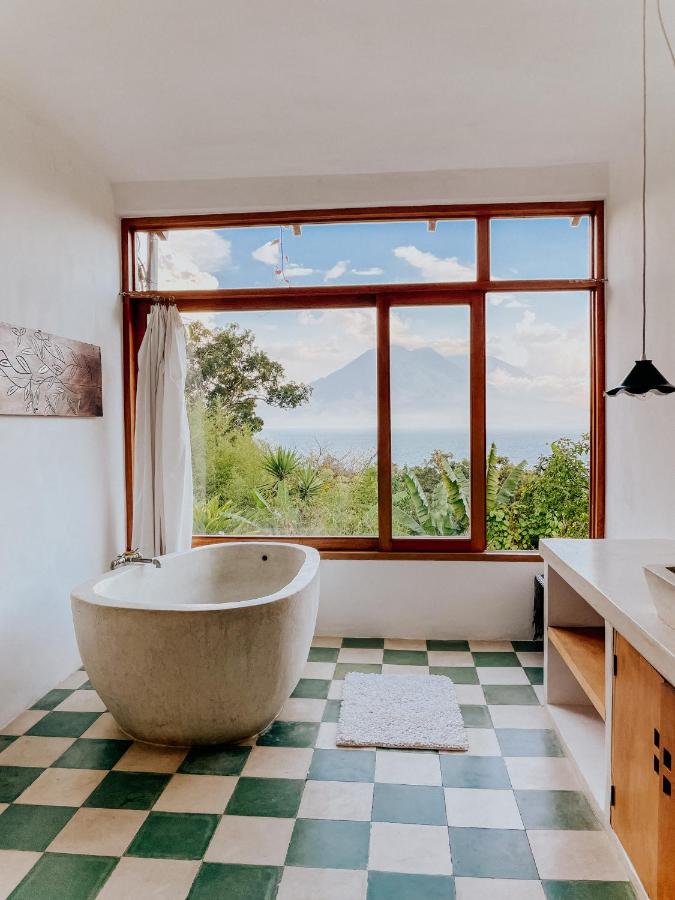 8 UNIQUE Places Where to Stay in Lake Atitlán 13 A modern bathroom with a freestanding white tub, green-and-white checkered tile floor, and a large window offering a scenic view—a perfect example of where to stay in Lake Atitlan for comfort and natural beauty.