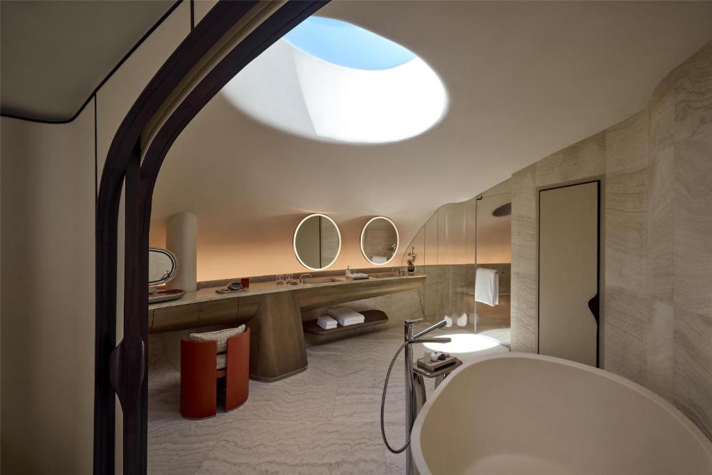 9 Best Hotels in Saudi Arabia: Unique Stays Across the Country 36 Modern bathroom with curved walls, a round skylight, freestanding bathtub, large vanity with two round mirrors, and warm ambient lighting—reminiscent of the elegant style found in the best hotels in Saudi Arabia.