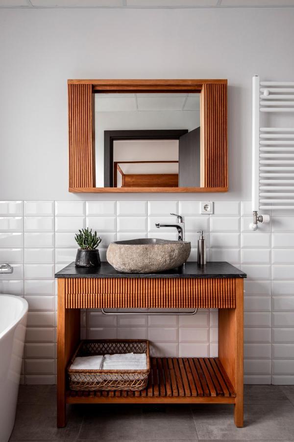 Where to Stay in Reykjavík: Top Guide 24 A modern bathroom, perfect inspiration for those seeking where to stay in Reykjavik, features a wooden vanity, stone vessel sink, potted plant, soap dispenser, rectangular mirror above white tiles, towel warmer on the wall, and a woven basket below.