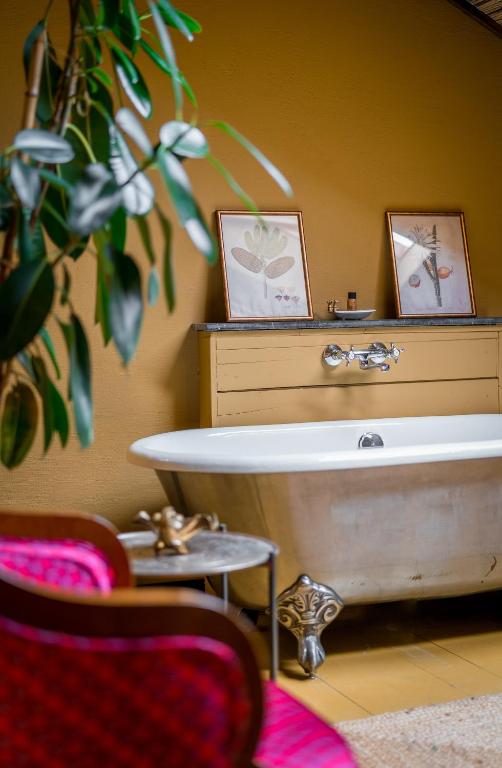 11 Unique Hotels in Georgia You Can't Miss! 43 A cozy bathroom with a vintage clawfoot bathtub, a wooden cabinet with botanical prints, a leafy plant, and a pink upholstered chair in the foregroundāperfect for those seeking inspiration from unique hotels in Georgia. The walls are painted a warm yellow color.