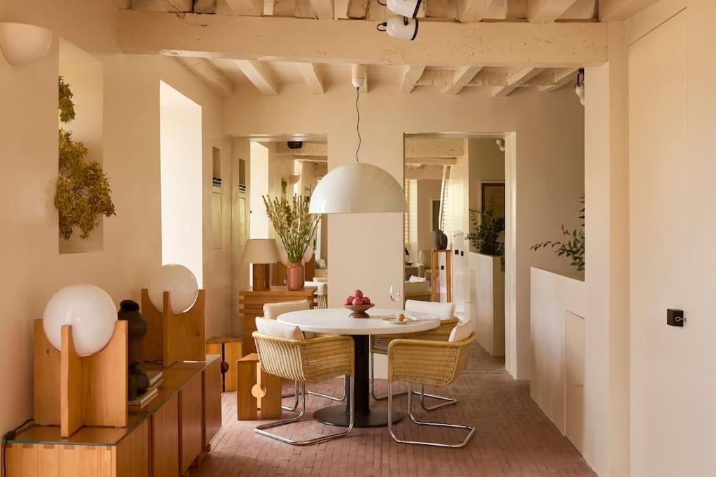 25 Weekend Trips from Madrid Max. 2h Away 58 A cozy dining area with a round white table, wicker chairs, a dome pendant lamp, and wooden furniture echoes the charming interiors found on weekend trips from Madrid, blending modern rustic style with warm neutrals and decorative plants.