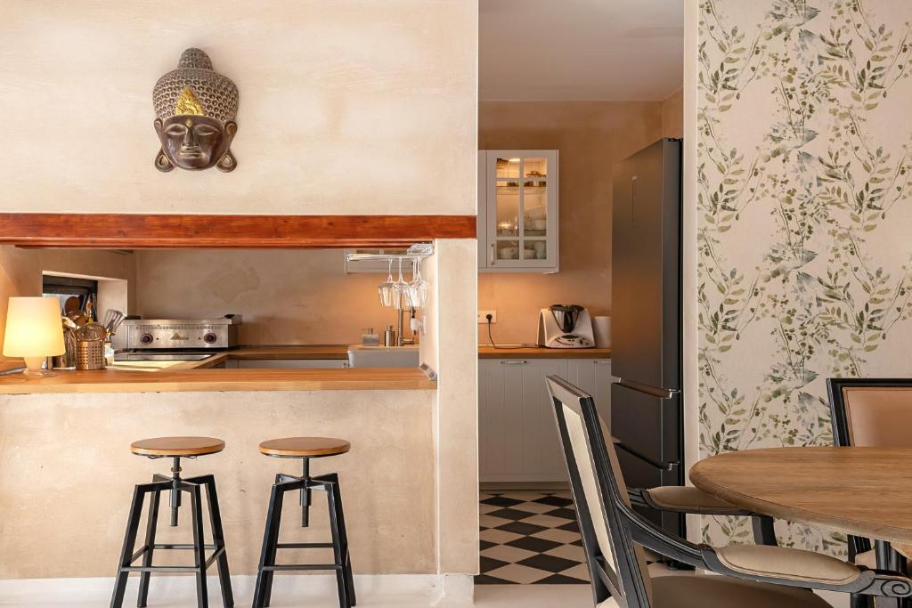 Adults Only Hotels in Fuerteventura 21 A cozy kitchen with beige walls, two black bar stools at a wooden counter, a Buddha head wall decor, and a dining table with chairs—reminiscent of the relaxed elegance found in adults only hotels in Fuerteventura.