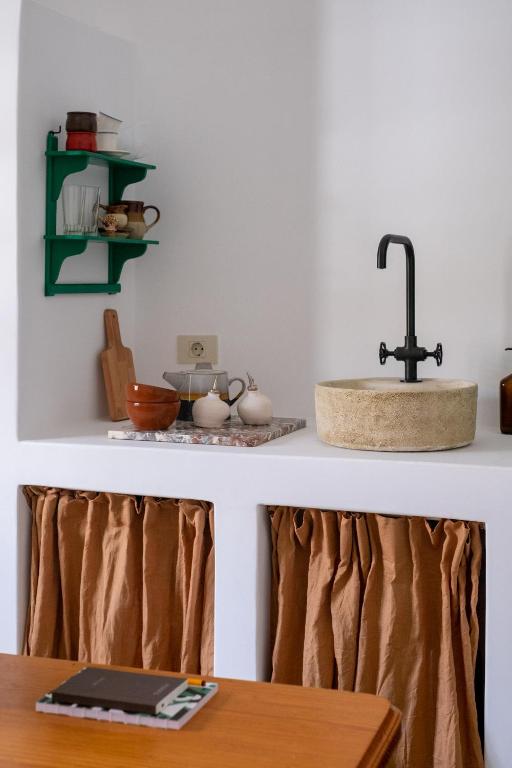 Unique Adults Only Hotels in Lanzarote 11 A small, minimalist kitchen nook with a round stone sink, black faucet, brown cloth curtains under the counter, and a green wall shelf—reminiscent of the cozy interiors found in Adults Only Hotels in Lanzarote.
