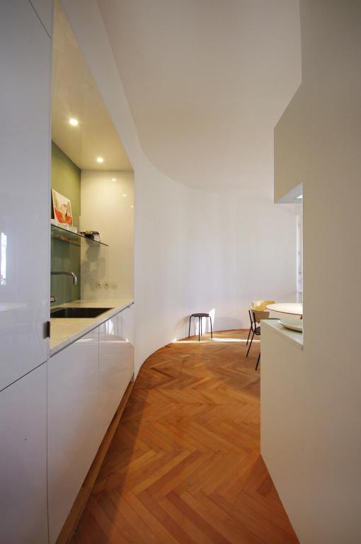 Where to Stay in Split: Hotel & Areas Guide 43 A modern kitchen with white cabinets, a curved wall, and wooden herringbone flooring, leading to a bright dining area—this minimalistic space is perfect inspiration for anyone searching Where to Stay in Split.