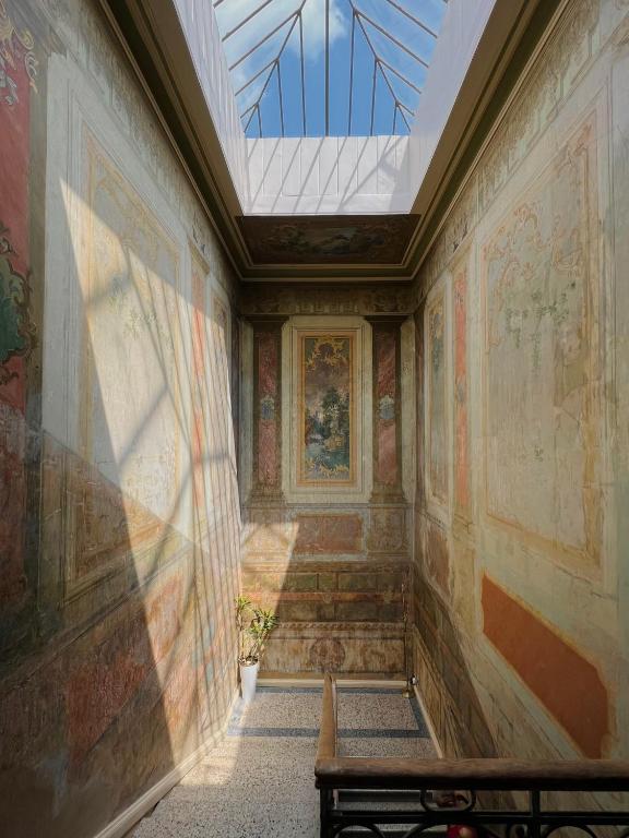 11 Unique Hotels in Georgia You Can't Miss! 6 A sunlit stairwell with ornate, faded wall murals and a glass ceilingāfeatures often found in unique hotels in Georgia. Shadows from the glass dance on the walls, while a small potted plant rests at the stairs' base beneath the blue sky above.