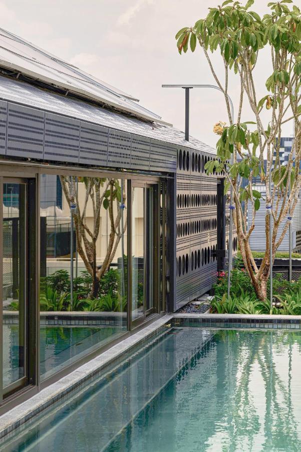 13 Most Unique Hotels in Singapore for an Incredible Holiday 32 A modern building with large glass windows beside a clear, rectangular swimming pool; trees and greenery are reflected in the glass, adding a natural touch to the contemporary architecture found in unique hotels in Singapore.