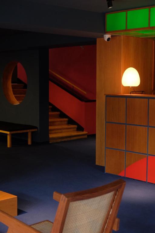 11 Unique Hotels in Georgia You Can't Miss! 12 A modern interior in one of the unique hotels in Georgia, featuring dark blue carpet, wooden furniture, a lit round lamp on a geometric-patterned reception desk, a red staircase, and a circular window in the wall.