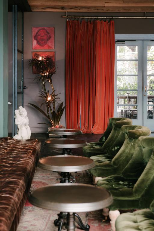 11 Unique Hotels in Georgia You Can't Miss! 16 A cozy lounge in one of the unique hotels in Georgia features green velvet chairs, round tables, a brown tufted sofa, white statue, orange curtains, two pink framed artworks, string-lit potted plant, and French doors with natural light.