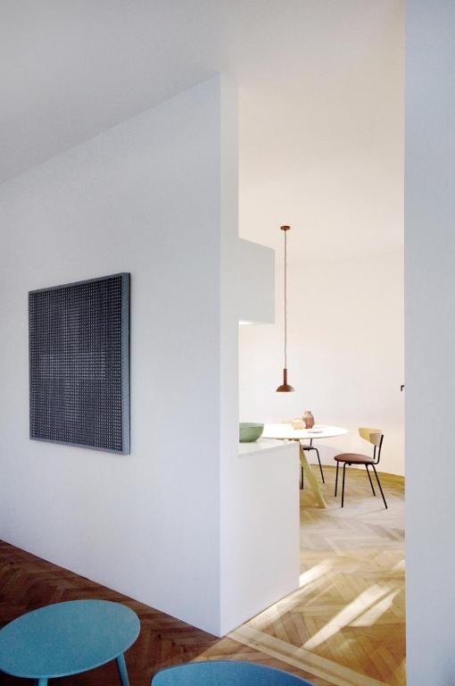 Where to Stay in Split: Hotel & Areas Guide 42 A modern, minimalistic interior showcases white walls, wooden floors, a small dining area with simple chairs and table, a hanging pendant light, and geometric artwork—an ideal inspiration for those searching Where to Stay in Split. Blue tables appear in the foreground.