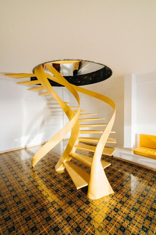 11 UNIQUE Boutique Hotels in Tenerife 12 Modern yellow spiral staircase with open steps and twisting supports, set in a room with patterned tile flooring, white walls, and a yellow bench—an interior style often found in boutique hotels in Tenerife.