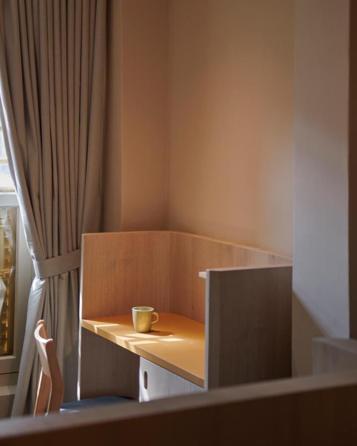 13 Most Unique Hotels in Singapore for an Incredible Holiday 11 A small wooden desk with a partition stands by a window with beige curtains, evoking the cozy charm found in unique hotels in Singapore. A single green mug rests on the desk, softly illuminated by sunlight.