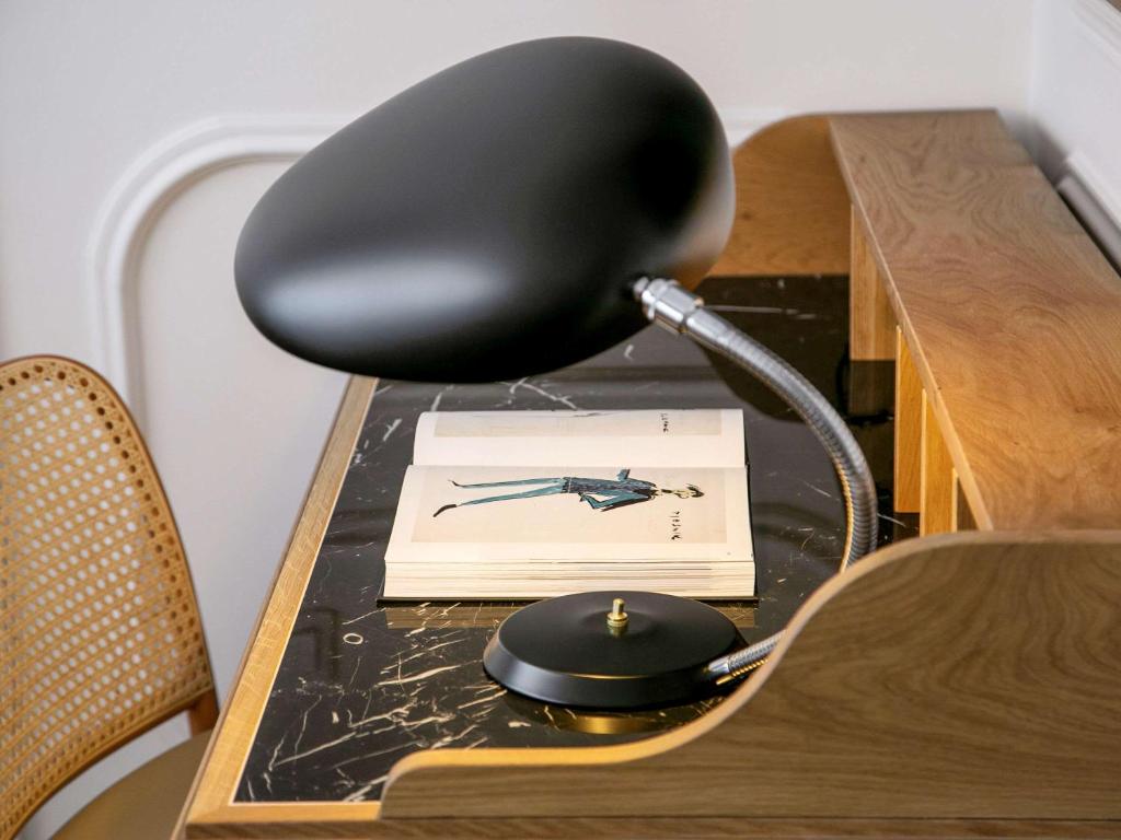 8 TOP Boutique Hotels in Split 9 A modern black desk lamp sits on a wooden desk with a black marble surface, next to a cane-backed chair—perfect inspiration while planning where to stay in Split. An open book with a fashion illustration lies beneath the lamp.