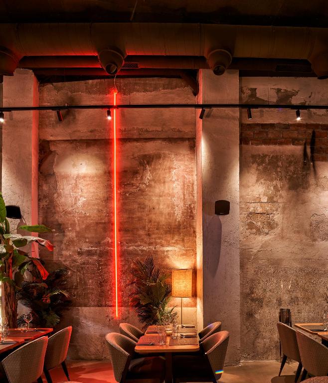 8 Unique Boutique Hotels in Bilbao Spain 11 A dimly lit restaurant interior inspired by boutique hotels in Bilbao, with rough textured concrete walls, red neon light accents, cozy seating, potted plants, and warm ambient lighting creating an inviting, modern atmosphere.
