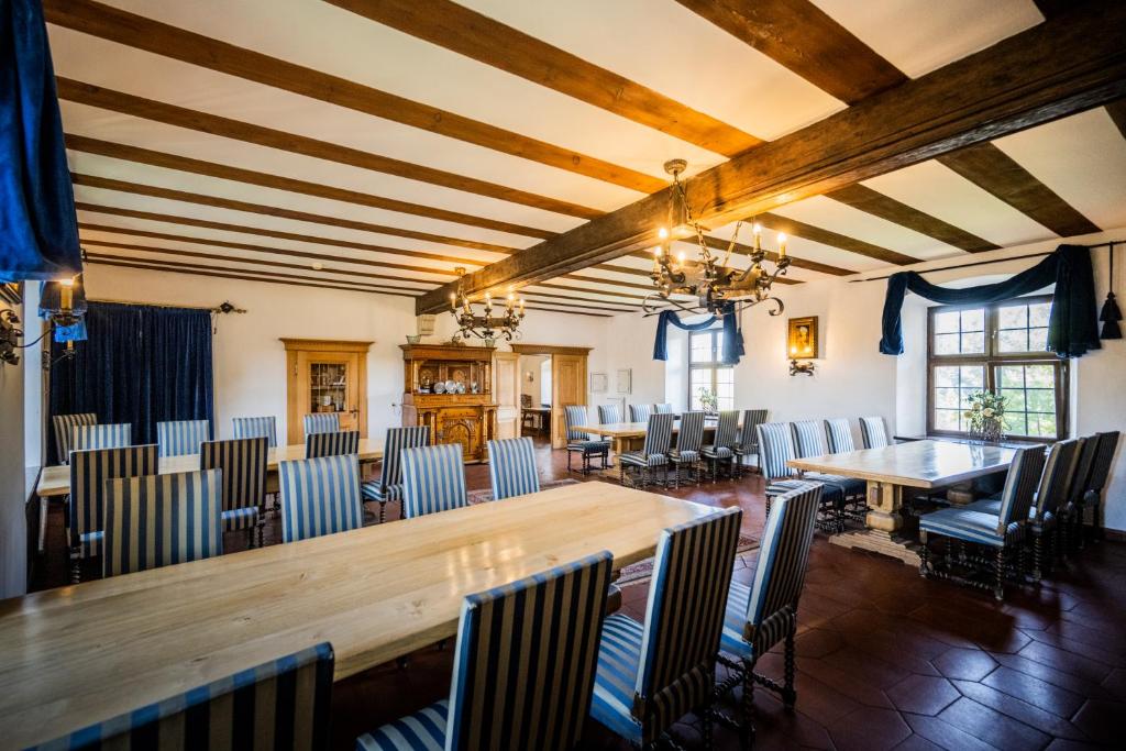 FAIRYTALE Castle Hotels in Bavaria 13 A spacious dining room in the style of castle hotels in Bavaria, featuring a wooden beam ceiling, striped upholstered chairs, long wooden tables, chandeliers, large windows with blue curtains, and a wooden cabinet against the wall.