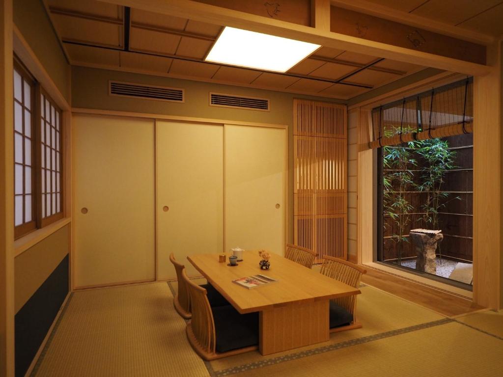 7 UNIQUE Ryokans in Gion Kyoto 3 A traditional Japanese tatami room, like those found in ryokans in Gion Kyoto, with a low wooden table, four chairs, sliding shoji doors, and a view of a small bamboo garden. The space features natural wood tones and soft lighting.