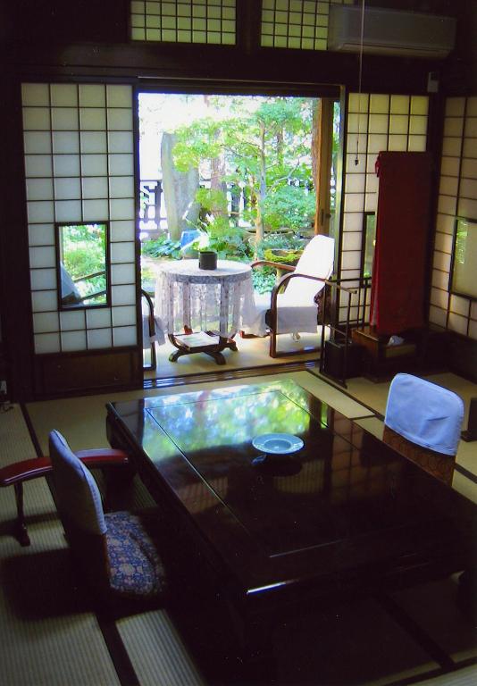 Looking for the Best Ryokan in Takayama? 8 A traditional Japanese room with tatami mats, a low wooden table, and chairs. Sliding shoji doors open to a garden view. Natural light fills this serene space, capturing the essence of the Best Ryokan in Takayama experience.