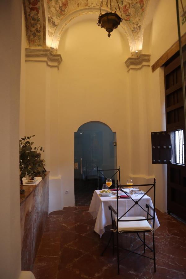 Best of Cordoba One Day Itinerary 5 A small dining table set for two with white tablecloths and drinks sits in an elegant room with high arched ceilings—perfect for a Cordoba one day experience—adorned with ornate decorations, warm lighting, a window, and a decorative ceiling.