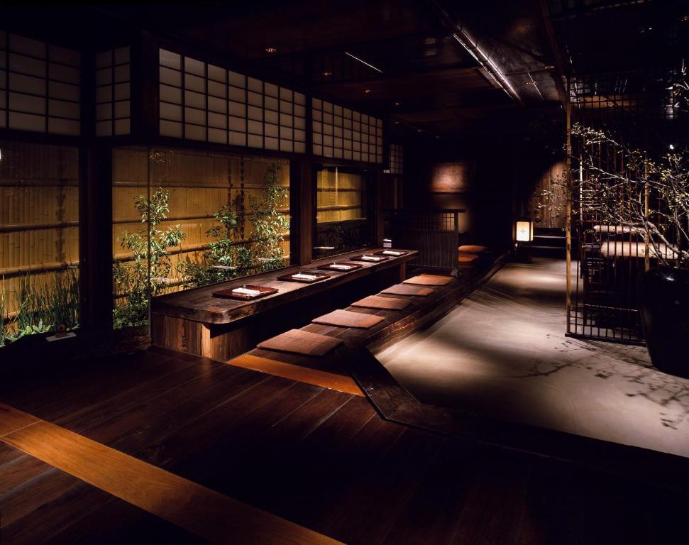7 UNIQUE Ryokans in Gion Kyoto 22 A dimly lit, elegant Japanese-style dining room inspired by ryokans in Gion Kyoto, with low wooden tables, floor cushions, shoji screens, bamboo plants outside the windows, and a minimalist, serene atmosphere.