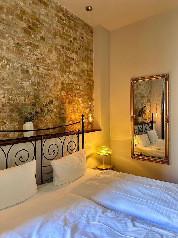 Boutique Hotels in Berlin Kreuzberg 31 A cozy bedroom reminiscent of boutique hotels in Berlin Kreuzberg, featuring a brick accent wall, a black metal bed frame with white bedding, a vintage mirror, warm lighting, and greenery on a wooden shelf for a relaxing atmosphere.