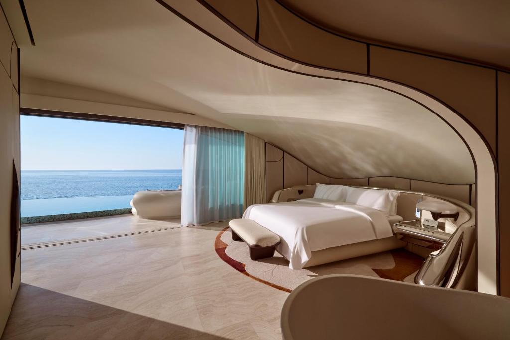 9 Best Hotels in Saudi Arabia: Unique Stays Across the Country 35 A modern, curved hotel room at one of the Best Hotels in Saudi Arabia, featuring a large bed, minimalistic furniture, and floor-to-ceiling windows with a clear ocean view and access to a sunlit terrace.