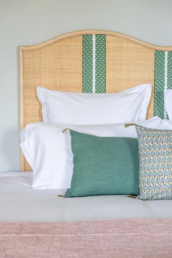 11 Unique Places to Stay in Provence 4 A neatly made bed with white pillows, a green cushion, and a patterned pillow rests against a wicker headboard with green vertical accents—capturing the charm of unique places to stay in Provence.