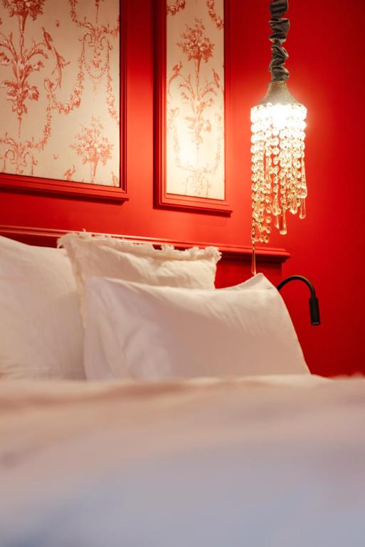Unique Boutique Hotels in Salzburg 8 A neatly made bed with white pillows and linens sits against a vibrant red wall with decorative patterns, reflecting the elegant charm found in boutique hotels in Salzburg. A chandelier-style light with hanging crystals is suspended above the bed.