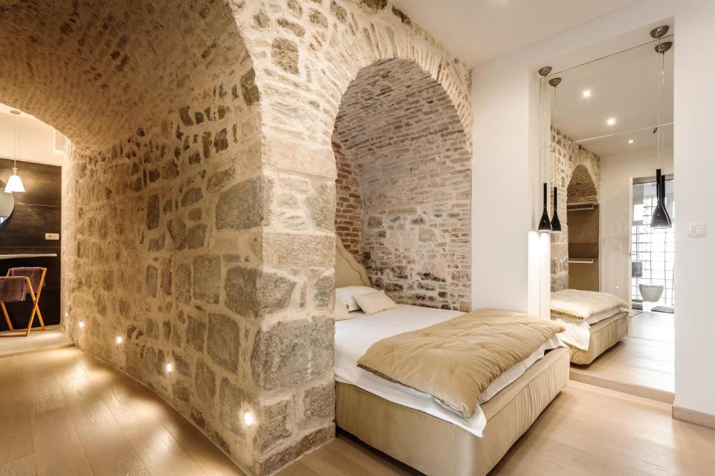 Where to Stay in Split: Hotel & Areas Guide 28 A cozy bedroom with exposed stone walls and arched ceilings, featuring a double bed with beige bedding, modern lighting, and wooden floors—an inviting choice for those searching Where to Stay in Split. Open view into a bathroom with a large mirror.