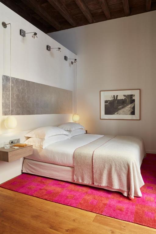 13 Unique Hotels in Barcelona, Spain 43 A modern bedroom inspired by Barcelona Hotels with Rooftop Pool, featuring a double bed in white and beige, globe lights, a floating nightstand, pink rug, wooden floors, and a framed black-and-white photo on the wall.