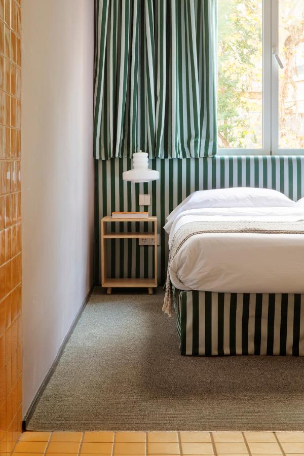 Where to Stay in Madrid: 14 Best Hotels 5 A neatly made bed with green and white vertical stripes on the headboard and curtains stands by a window; if you're wondering where to stay in Madrid first time, this inviting room features a modern white lamp on a nightstand and orange tiles along the floor edge.