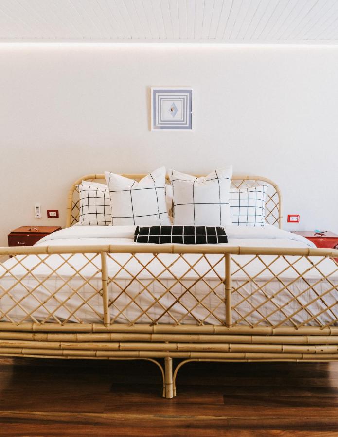 Unique Hotels in Costa Rica: Top Stays 14 A neatly made bed with a woven rattan frame, two white pillows with black grid patterns, a black checked throw, and wooden nightstands embodies the chic, airy style you’ll find at unique hotels in Costa Rica, complete with small framed wall art above.