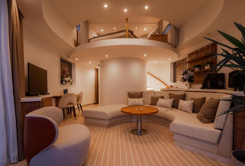 Where to Stay in Split: Hotel & Areas Guide 36 A modern, warmly-lit living room—perfect for those seeking where to stay in Split—features a curved beige sofa, round wooden coffee table, flat-screen TV, and a mezzanine bedroom above, accessible by a spiral staircase. Neutral tones add cozy accents.
