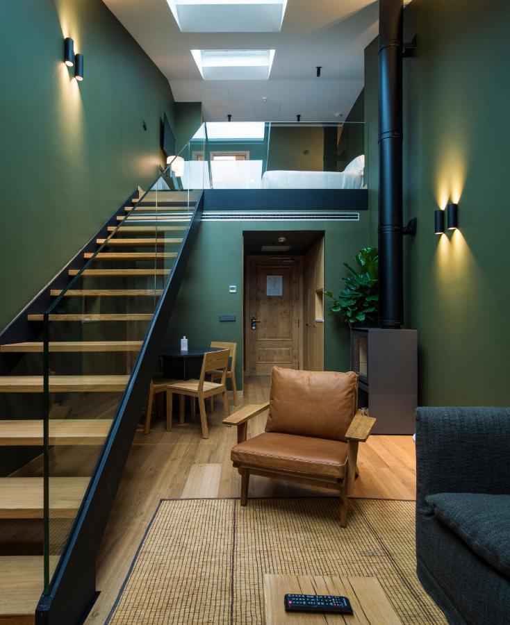 Best Boutique Hotels in San Sebastian 9 A modern duplex living space inspired by boutique hotels in San Sebastian, with green walls, wooden floors, a brown armchair, glass-railed staircase, loft bed area, skylights, and cozy lighting for a warm atmosphere.