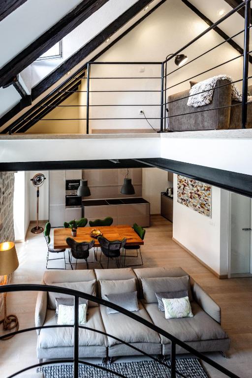 Where to Stay in Split: Hotel & Areas Guide 27 Modern loft apartment with exposed beams, a mezzanine couch, and an open-plan living area below—perfect for those seeking Where to Stay in Split. Enjoy a dining table, kitchen, and cozy seating with two sofas and decorative pillows.