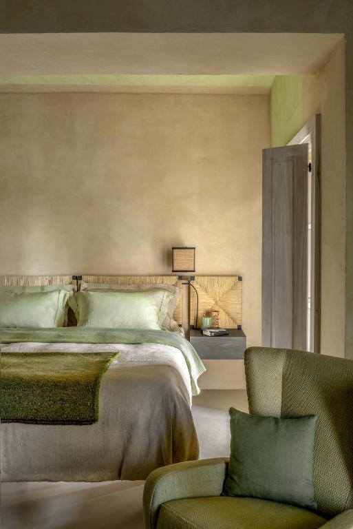 7 Best Agriturismos in Tuscany 7 A cozy bedroom reminiscent of the best agriturismos in Tuscany, with a bed dressed in light green and beige bedding, a green armchair with a matching pillow, and a nightstand with a lamp beside a partially open door.