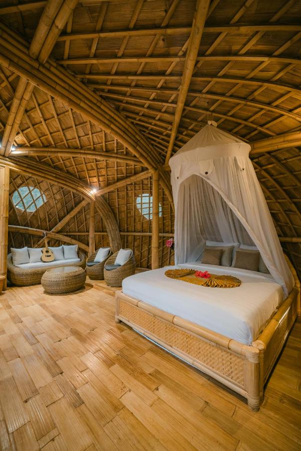 A cozy bamboo bedroom with a thatched arched ceiling, a bed with a white canopy, wicker chairs, and warm lighting—perfect for relaxing in one of the best family villas in Bali.