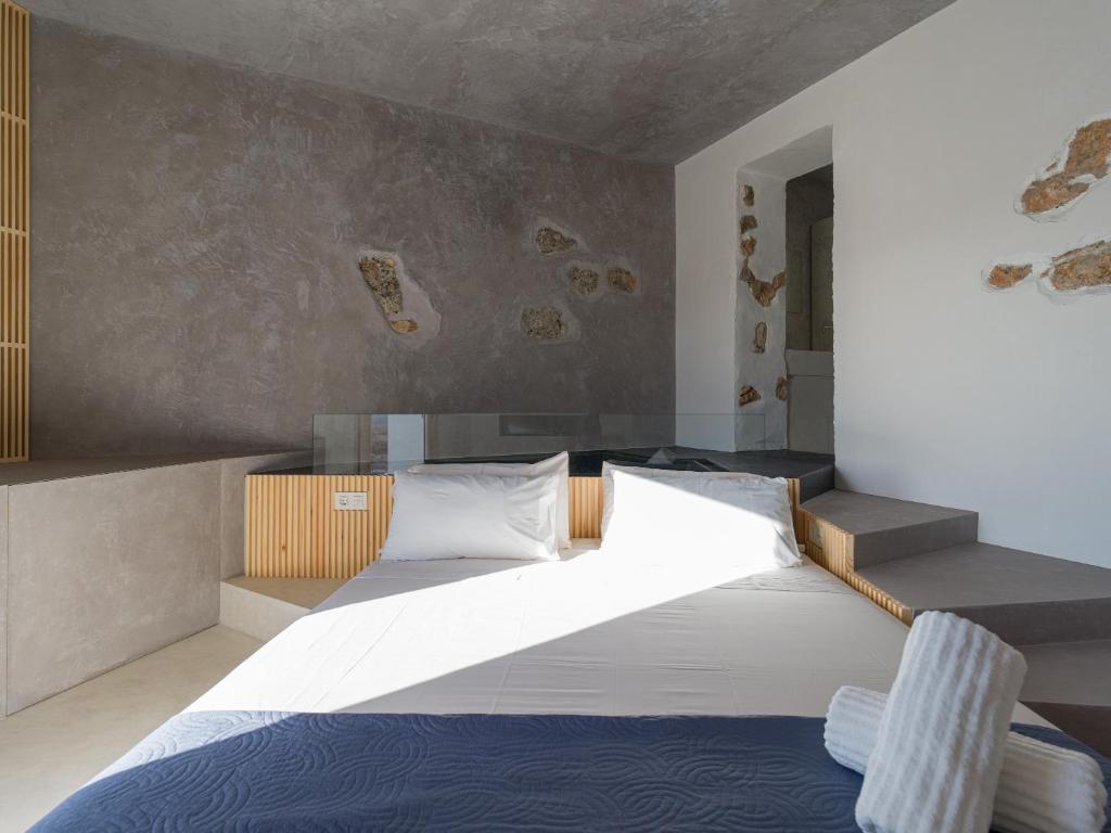 Adults Only Hotels in Fuerteventura 7 Modern minimalist bedroom with a built-in bed, white and gray bedding, a rolled towel, natural stone accents on the walls, and concrete textures—typical of adults only hotels in Fuerteventura. Sunlight streams in, creating a bright and airy atmosphere.