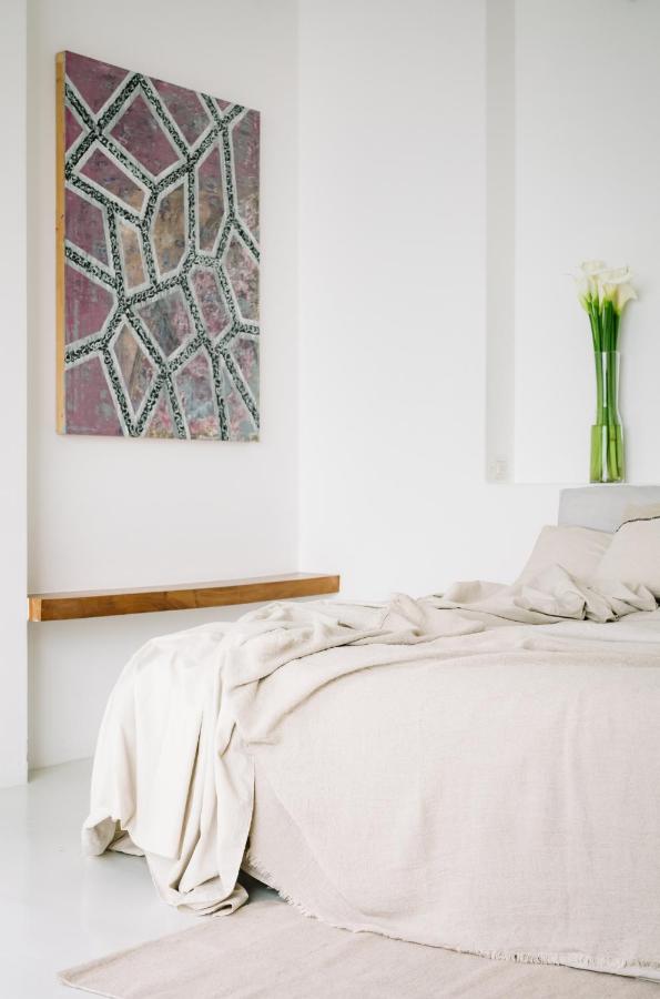 8 UNIQUE Places Where to Stay in Lake Atitlán 6 Minimalist bedroom with a beige bed, draped blanket, modern geometric painting, and a vase of white calla lilies—inviting decor ideas for those seeking inspiration on where to stay in Lake Atitlan.