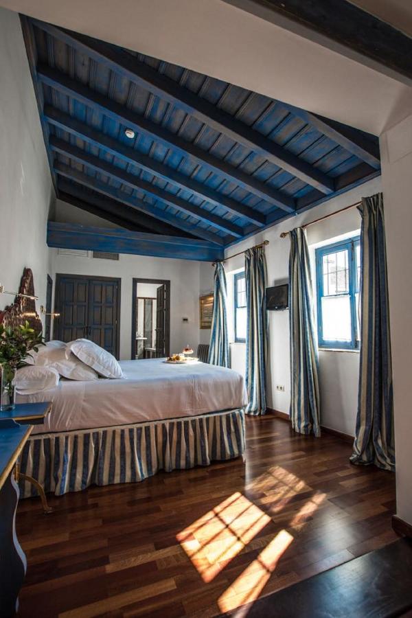 Best of Cordoba One Day Itinerary 2 A cozy bedroom with a blue vaulted ceiling, striped curtains and bed skirt, wooden floors, and sunlight streaming in—perfect for relaxing after exploring Cordoba one day.