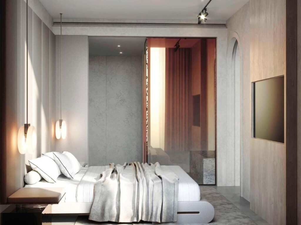 13 Most Unique Hotels in Singapore for an Incredible Holiday 50 A modern, minimalist bedroom inspired by unique hotels in Singapore features a low platform bed, white bedding, pendant lights, neutral-toned walls, a large wall-mounted TV, and a glass partition revealing a warmly lit area beyond.