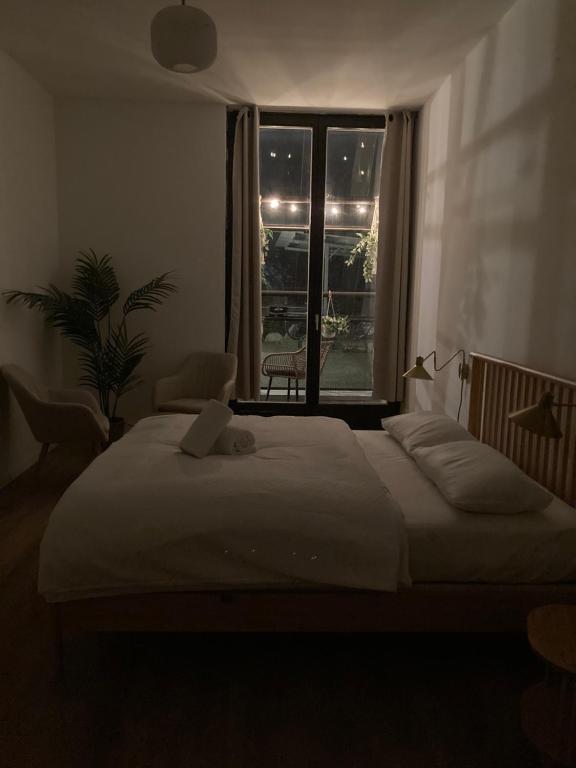 Boutique Hotels in Berlin Kreuzberg 38 A dimly lit bedroom, typical of boutique hotels in Berlin Kreuzberg, features a neatly made bed, two armchairs, a potted plant, and a large window with curtains overlooking a balcony adorned with string lights at night.