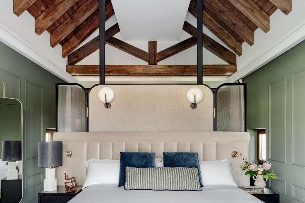 8 Unique Boutique Hotels in Bilbao Spain 25 A modern bedroom inspired by boutique hotels in Bilbao, featuring a high vaulted wooden ceiling, green paneled walls, a padded beige headboard, dark bedside tables with lamps, decorative pillows, and wall-mounted round lights above the bed.