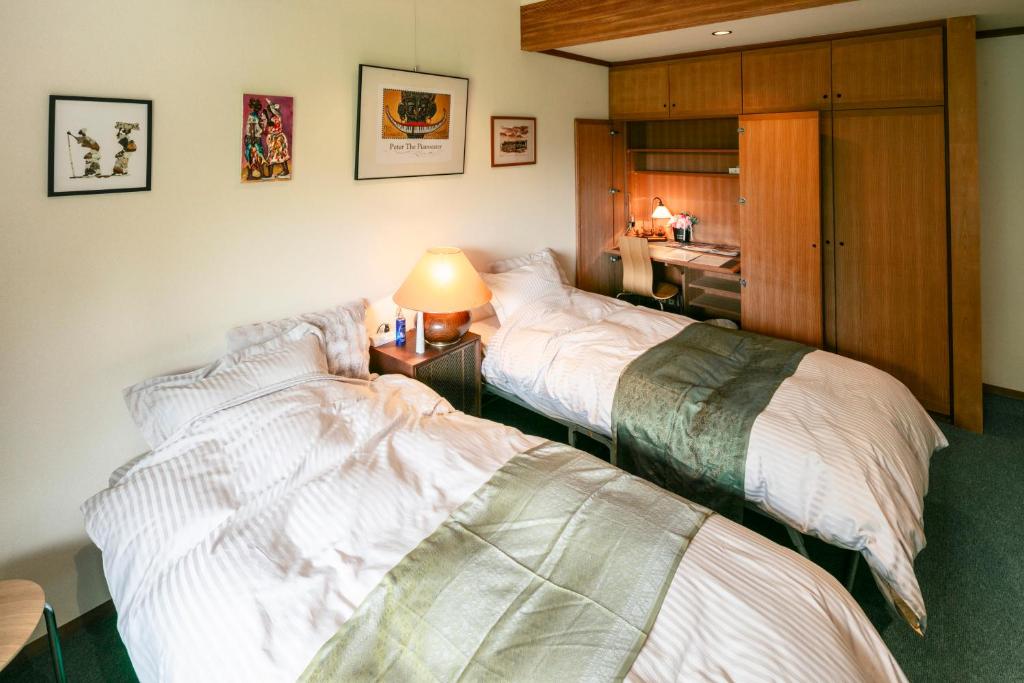 8 BEST Ryokans in Osaka 24 A cozy bedroom inspired by ryokans in Osaka, featuring two single beds with white striped bedding and green throws, a bedside table with a lamp, wall art above the beds, and a wooden wardrobe with a small desk area.