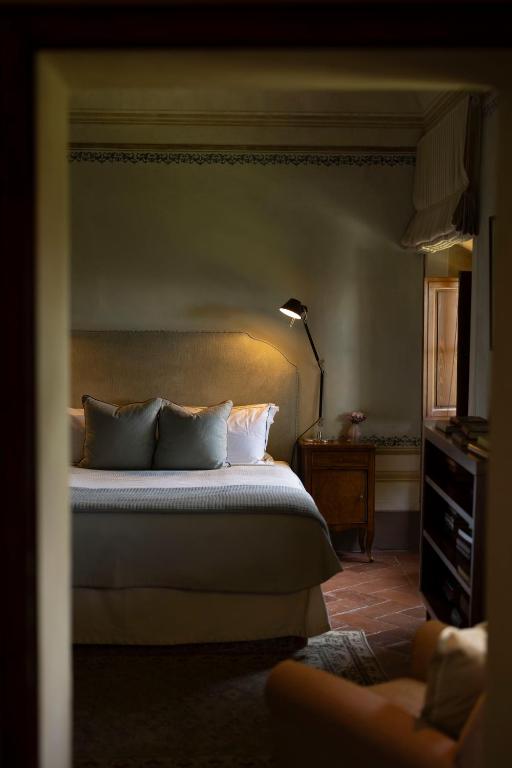 7 Best Agriturismos in Tuscany 24 A cozy bedroom inspired by agriturismos in Tuscany, with a neatly made bed with blue pillows, a bedside table with a lamp, a sunlit window, and a bookshelf, all viewed from an adjacent room through an open doorway.