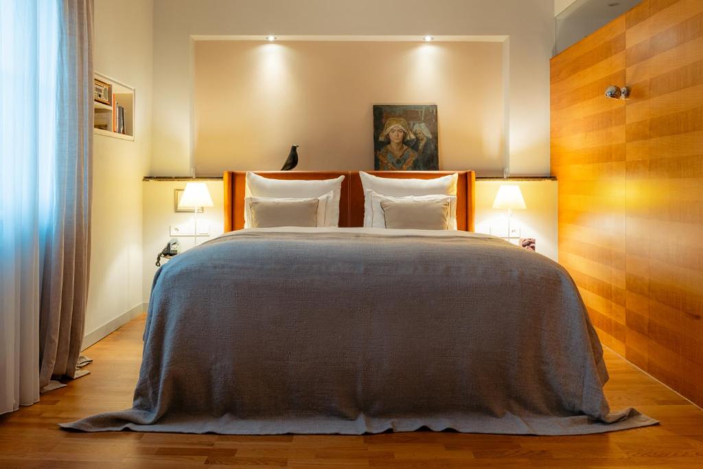 Unique Boutique Hotels in Salzburg 30 A cozy bedroom reminiscent of boutique hotels in Salzburg, featuring a large bed with a gray blanket, two white pillows, bedside tables with lamps, warm wooden flooring, and a framed painting above the headboard.