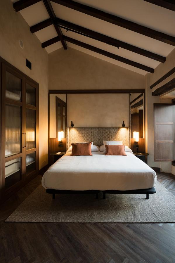 25 Weekend Trips from Madrid Max. 2h Away 94 A cozy bedroom perfect for weekend trips from Madrid, featuring a large bed with white linens, orange pillows, wooden ceiling beams, mirrored closets, and soft lighting that creates a warm, inviting atmosphere.