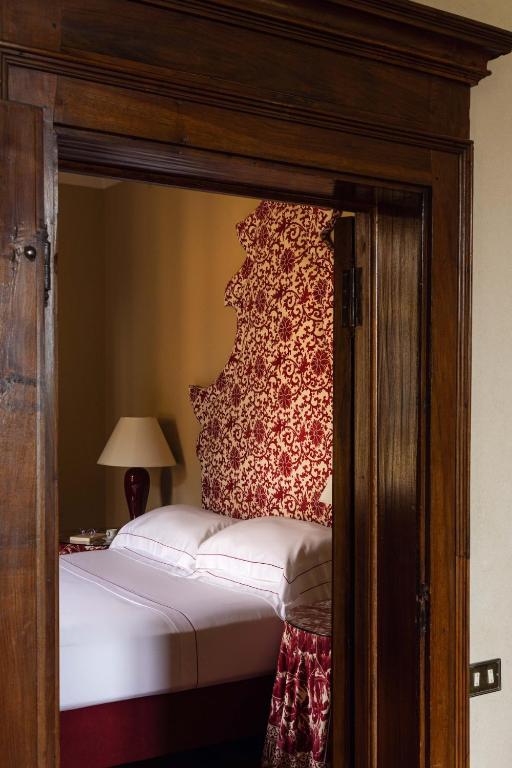 7 Best Agriturismos in Tuscany 11 View through a wooden doorway into a cozy bedroom—like those found at the best agriturismos in Tuscany—with a bed featuring a red and white patterned headboard, matching bedding, and a bedside table with a lamp.