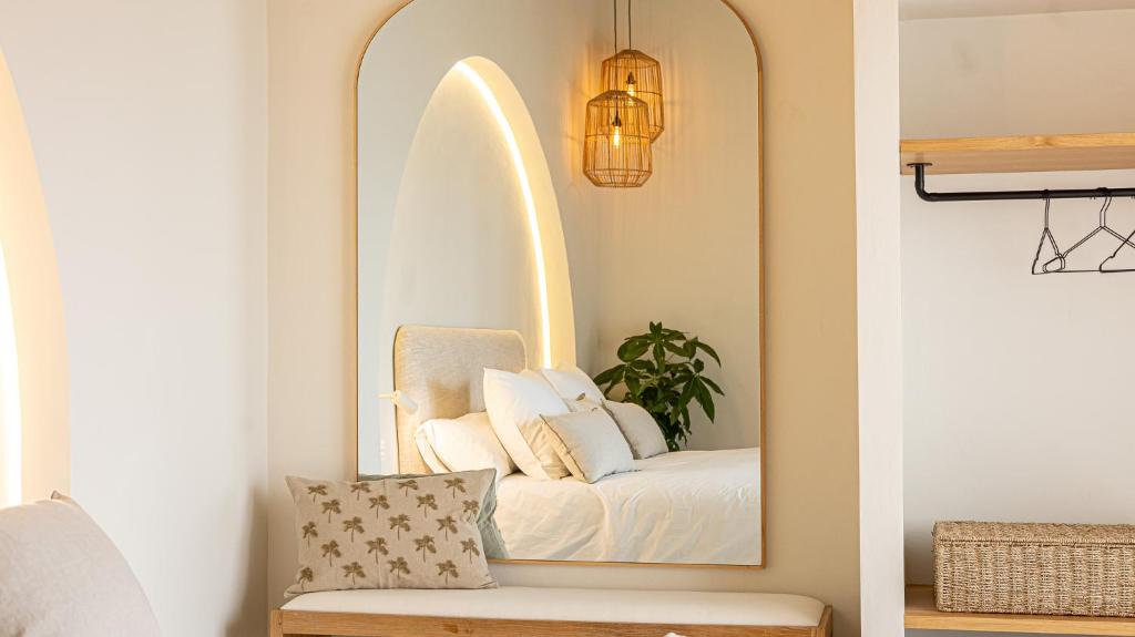 Adults-Only Hotels in Costa del Sol 4 A large arched mirror reflects a cozy bed with white bedding, hanging pendant lights, and a green plant—echoing the serene style found in adult only hotels in Costa del sol. A bench with a patterned cushion and wicker basket sits nearby in the open closet area.