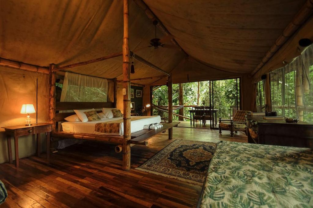 Unique Hotels in Costa Rica: Top Stays 10 A rustic, spacious cabin bedroom with bamboo furniture, a canopy bed, and large windows revealing lush forest—a tranquil retreat that stands out among unique hotels in Costa Rica. Warm lighting and cozy decor complete the peaceful ambiance.