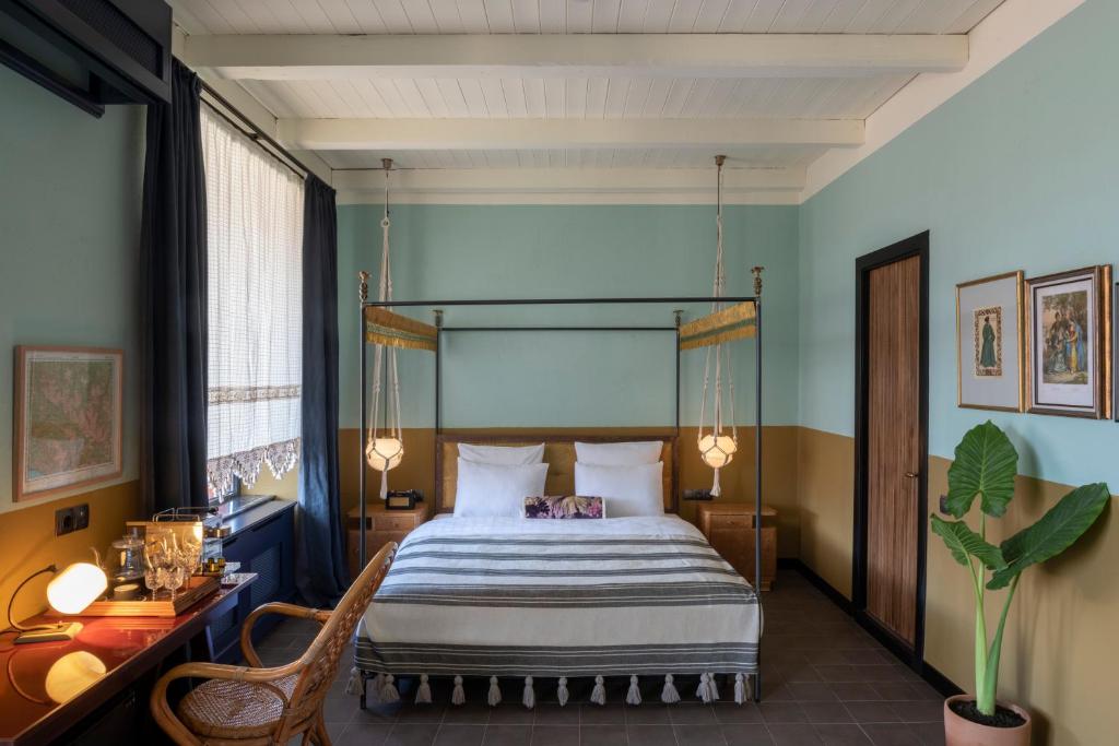 11 Unique Hotels in Georgia You Can't Miss! 42 A cozy bedroom in the style of unique hotels in Georgia, featuring a four-poster bed, white and striped bedding, pendant lights, a wooden desk with chair, green and tan walls, framed artwork, and a large leafy plant in the corner.